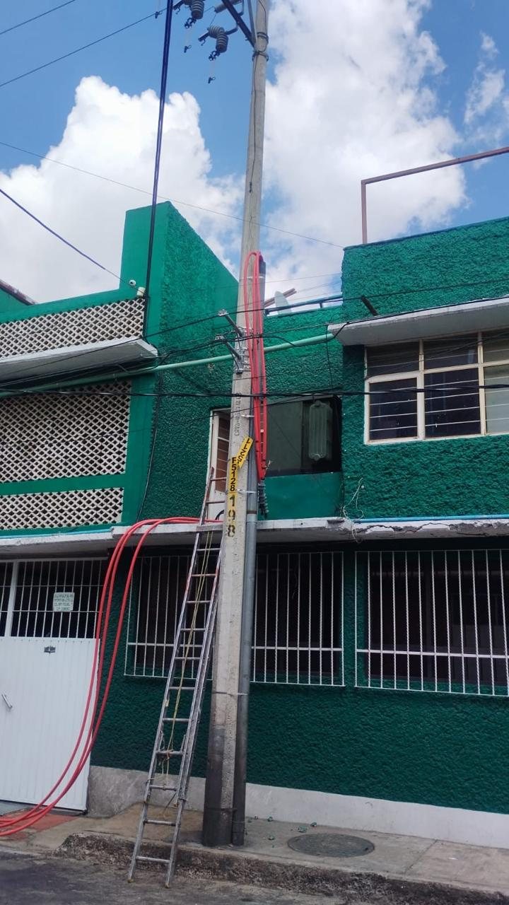 Poste con acometida eléctrica y escalera de trabajo frente a una casa